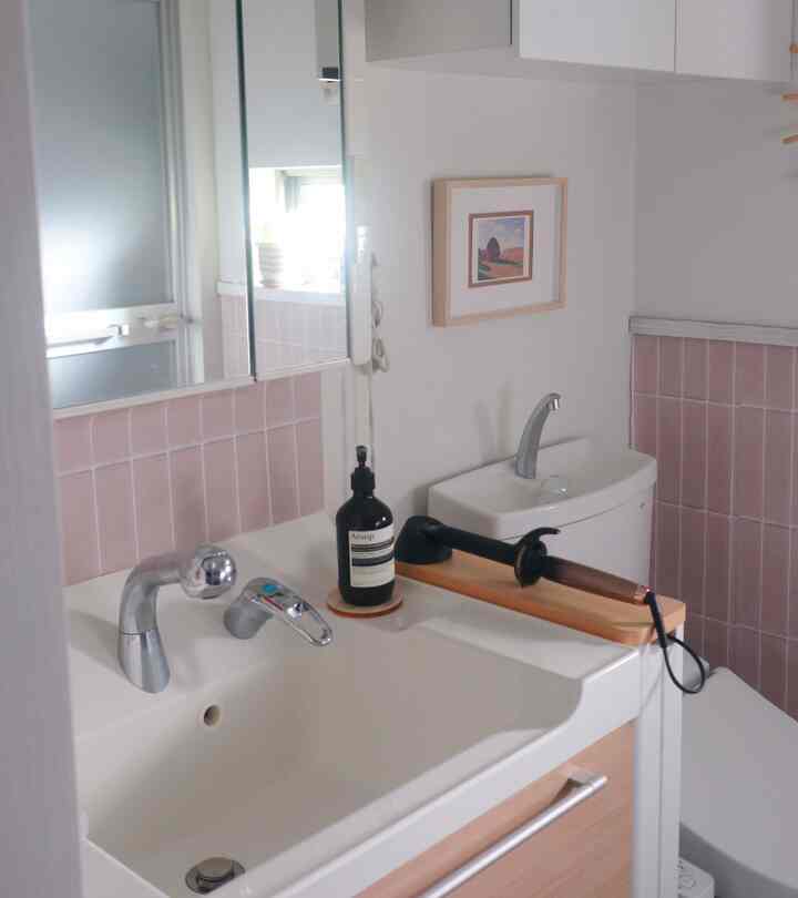 白とピンクのタイルが調和する小さなトイレ、洗面台と便器が整然と配置されたシンプルでモダンなインテリア