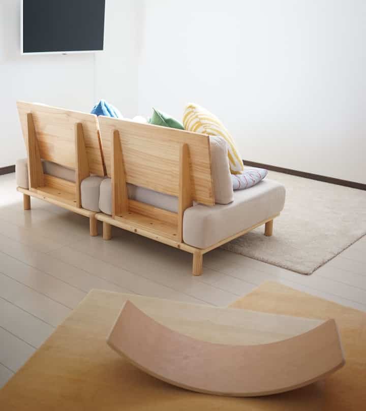 ナチュラルな色調のリビング、木製ソファとベージュのラグが配置されたシンプルで明るいインテリア