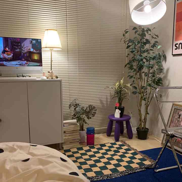 Natural-toned small living room featuring white cabinet, floor lamp, purple stool, and plants creating a simple cozy space