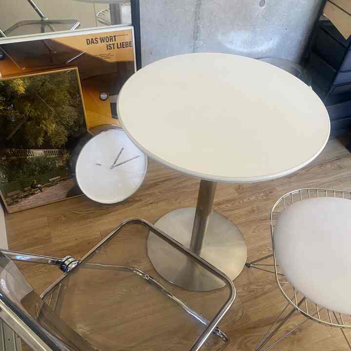 木目調の床が特徴的なカフェ風の小さな空間に透明な椅子と白い円形のサイドテーブルが配置されている