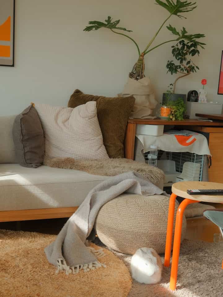 Natural beige-toned living room featuring a beige sofa, stool, cushions, and blankets creating a cozy atmosphere