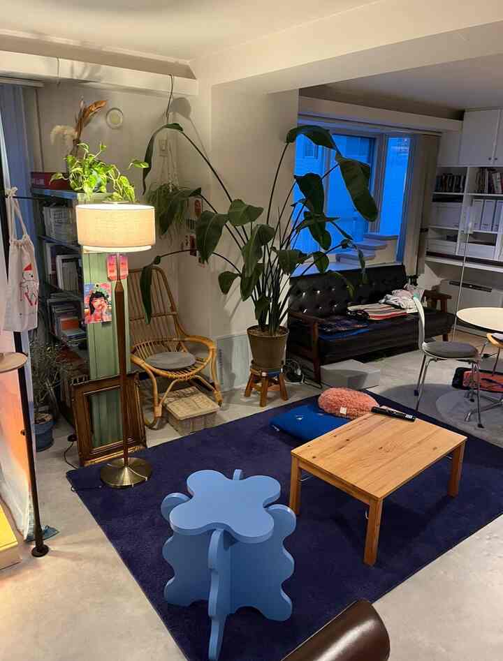 ブルーのカーペットとナチュラルウッドの家具、黒いレザーソファが配置された雰囲気のあるリビング