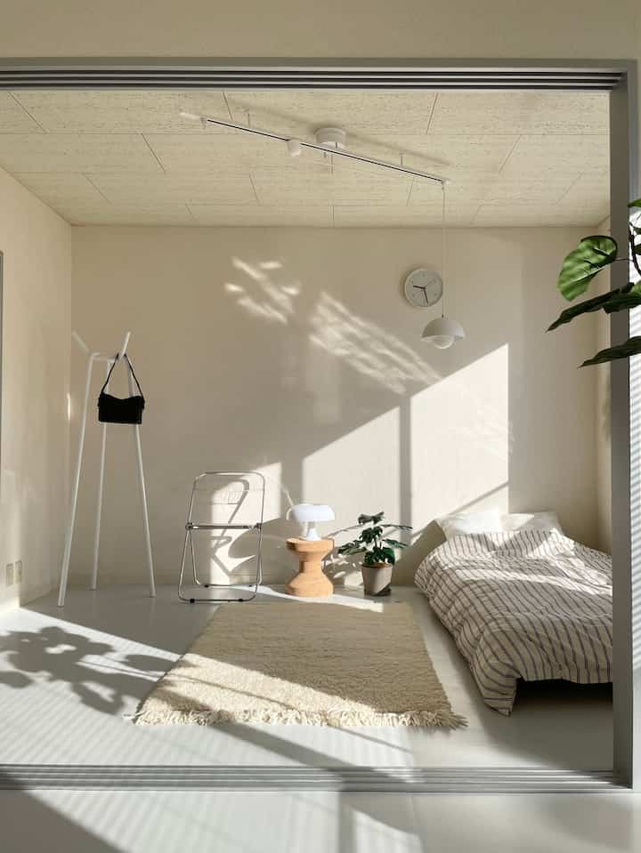 ナチュラルな色調の壁と床、シンプルな家具とベッドが配置された朝の光が差し込む落ち着いた寝室空間