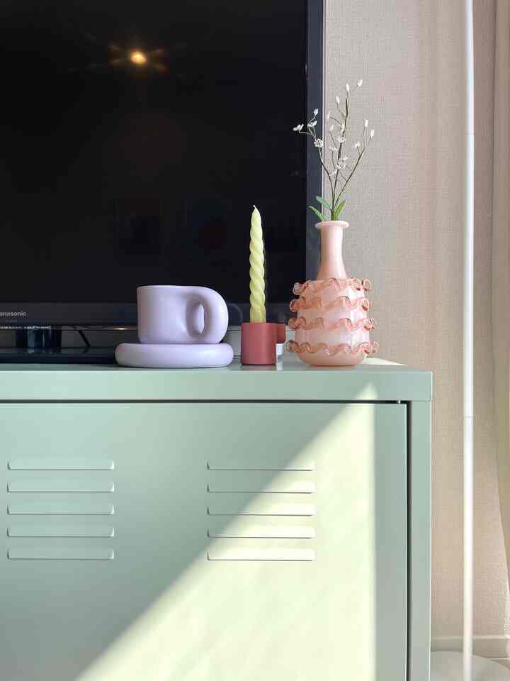 Simple living room featuring a pastel green cabinet with a TV, twisted candle, and vase with flowers in soft natural tones