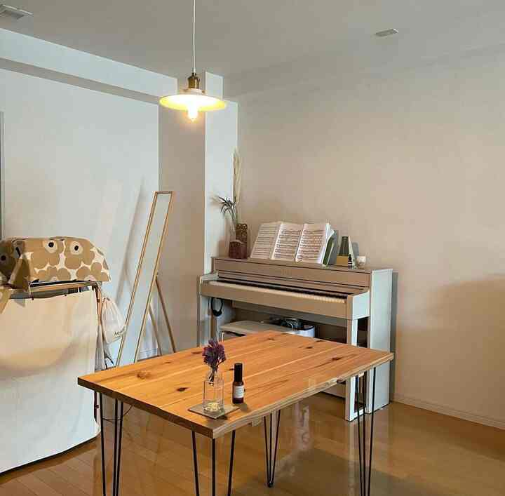 Bright natural-toned studio apartment featuring a wooden table centrally and a white digital piano on the right side in an inviting interior