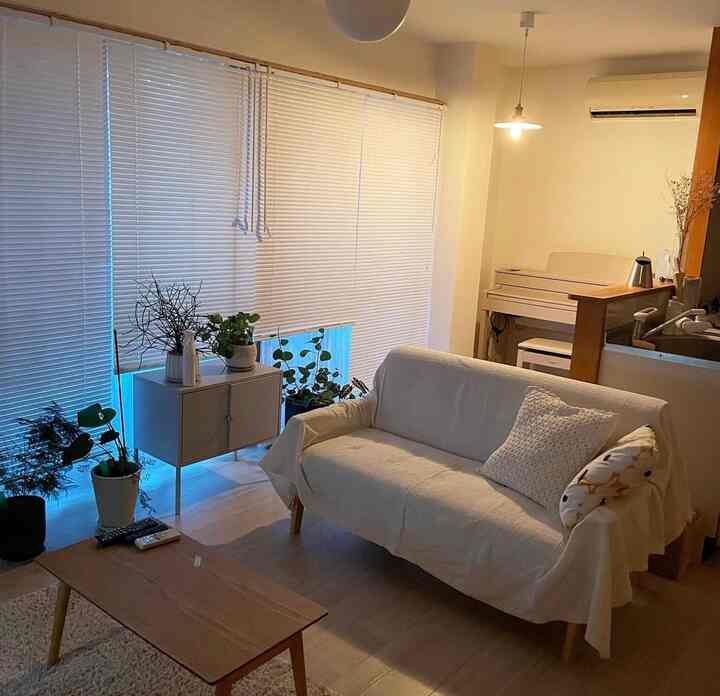 白と木目調の2LDKリビング、清潔感のあるソファとコーヒーテーブル、ブラインドと植物が配置された落ち着いた雰囲気の空間