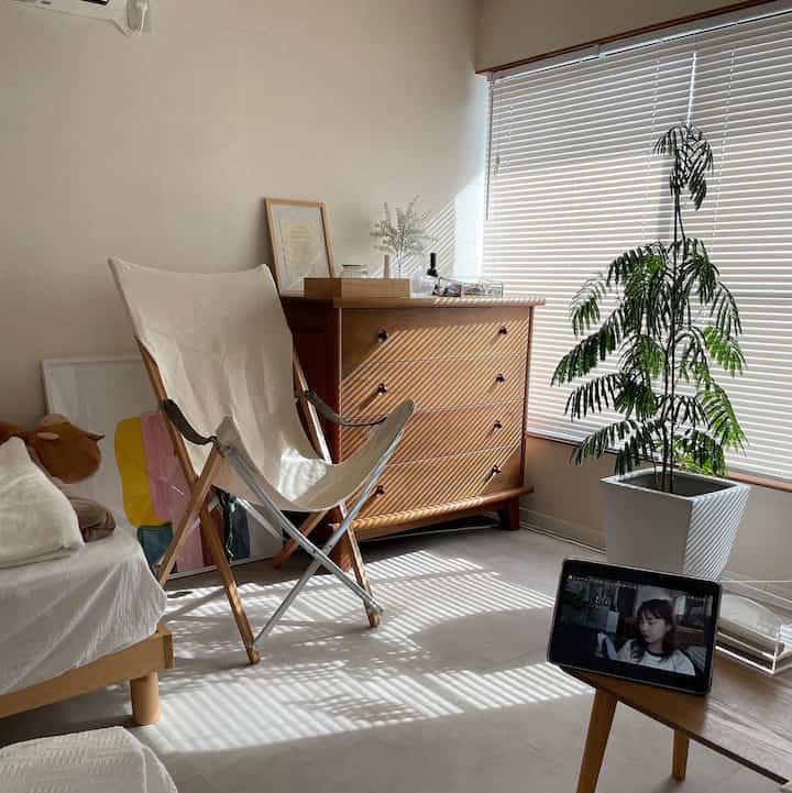 A small living room in warm ivory and light brown tones, featuring a cozy canvas chair and wooden dresser creating a natural ambiance