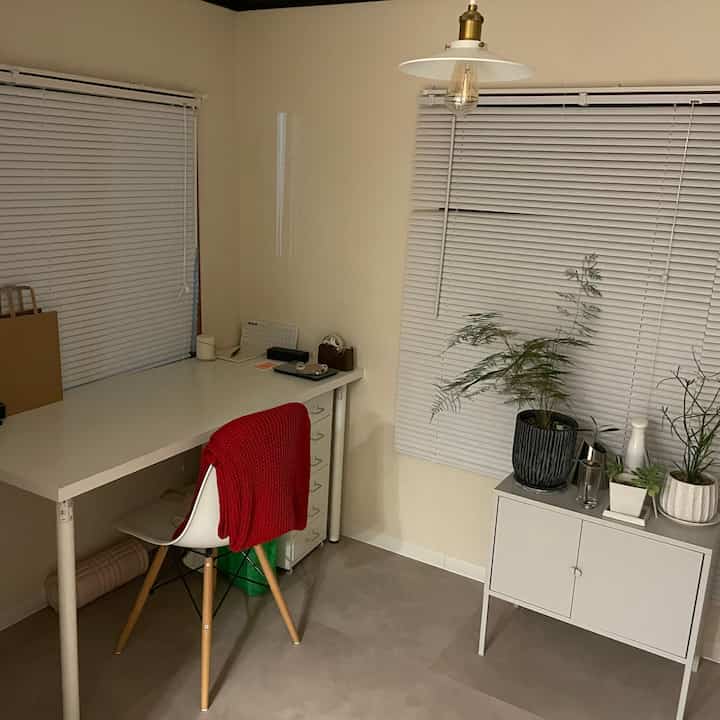 Compact home office in white and gray tones featuring a clean desk, drawer unit, and potted plants with a simple atmosphere