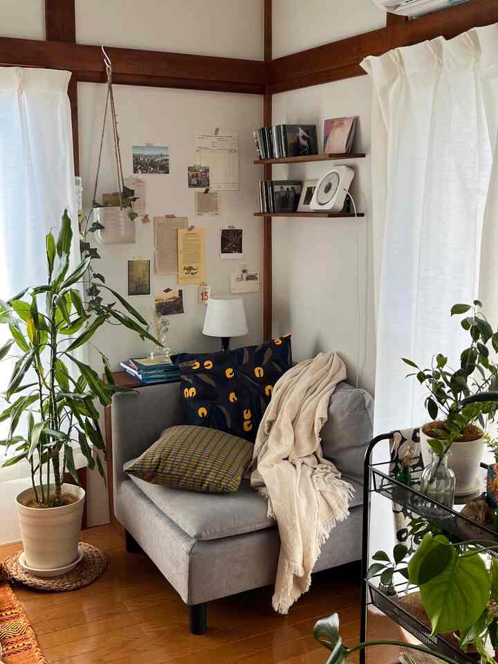 ナチュラルな色調の小さなリビングに、グレーの一人掛けソファと多くの植物が置かれた雰囲気のある読書コーナー