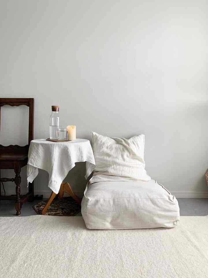 白とナチュラルな色調のリビング、ゆったりとしたクッションとサイドテーブル、ヴィンテージチェアが配置された雰囲気のある空間