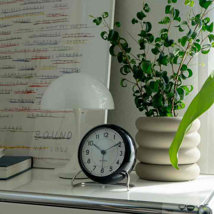 White and gray toned sideboard featuring an Arne Jacobsen clock, table lamp, and plant in a mid-century modern style setting