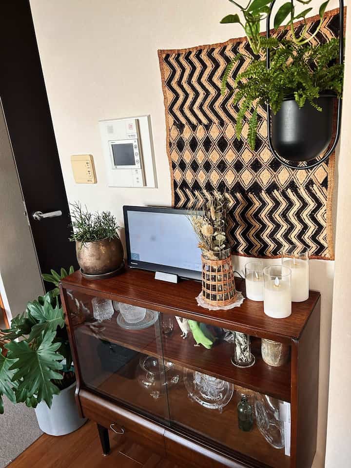 ブラウンを基調としたリビング、ヴィンテージの木製キャビネットと多様な植物、キャンドルが配置されたナチュラルな雰囲気のインテリア