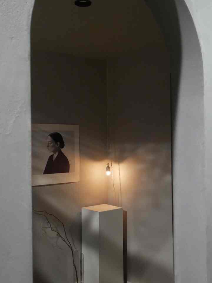 Gray-walled entrance space framed by white arch, featuring a pendant light and art poster with a minimalist interior style