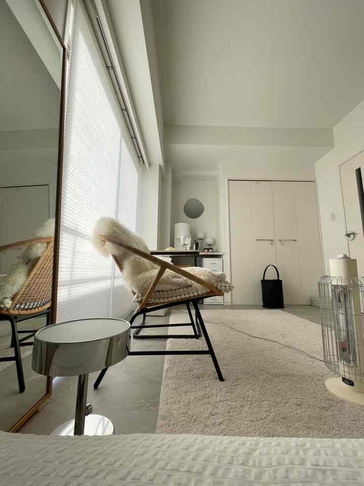 明るいホワイトトーンのワンルーム、自然素材のアームチェアとベージュのカーペットが配置された、すっきりとした雰囲気のある空間