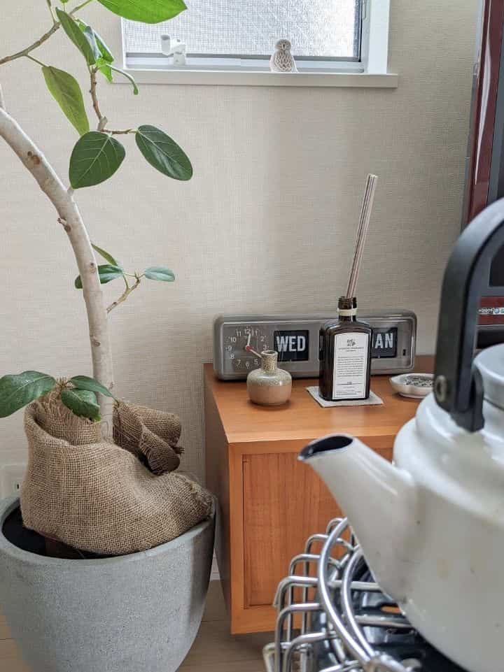 ベージュの壁と木目調の家具が配置されたナチュラルな空間、観葉植物とディフューザー、フリップクロックが調和する雰囲気のあるインテリア