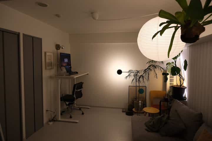 明るいホワイトトーンの壁と床にグレーのソファと植物が調和したモダンなリビング兼ホームオフィススペース