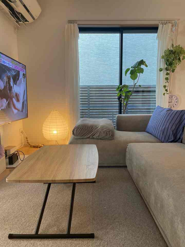 A cozy living room with gray and wood tones featuring a sofa, folding coffee table, and plants near large windows