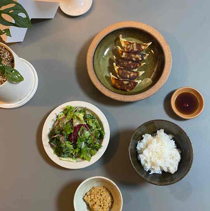 ナチュラルカラーのテーブルに配置された焼き餃子、ご飯、サラダ、納豆などの食事セット