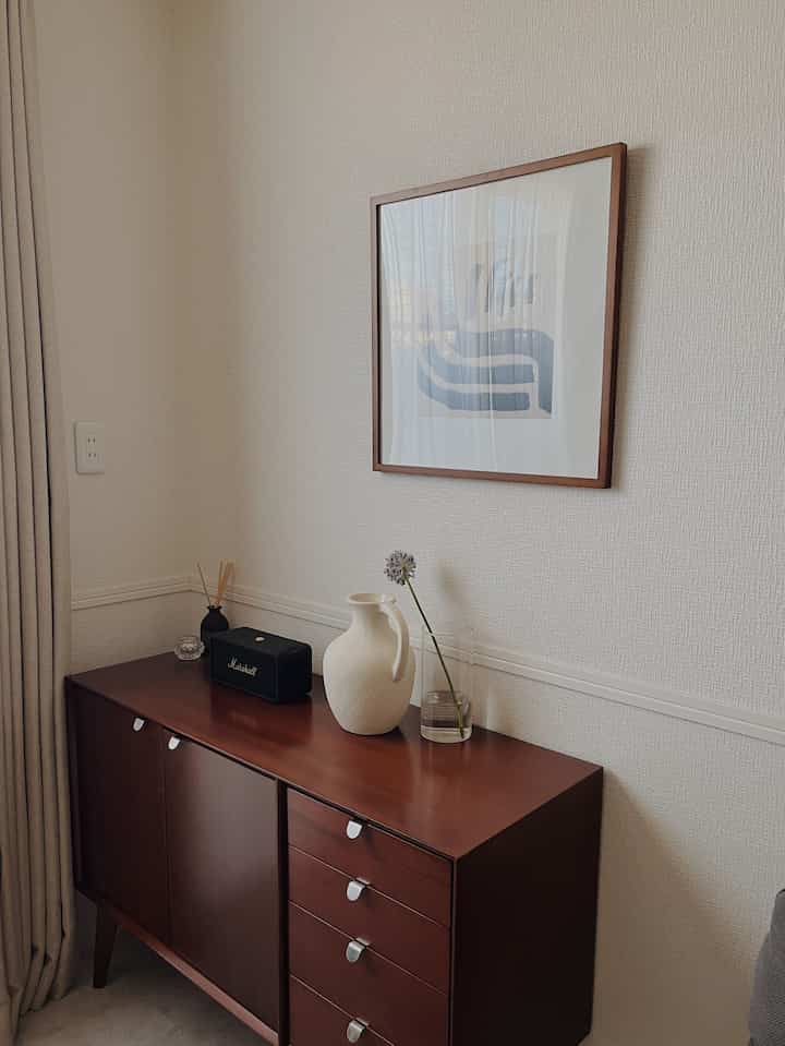 ブラウンの木目調サイドボードと白い壁、ポスターが配置された北欧スタイルの落ち着いたリビング空間