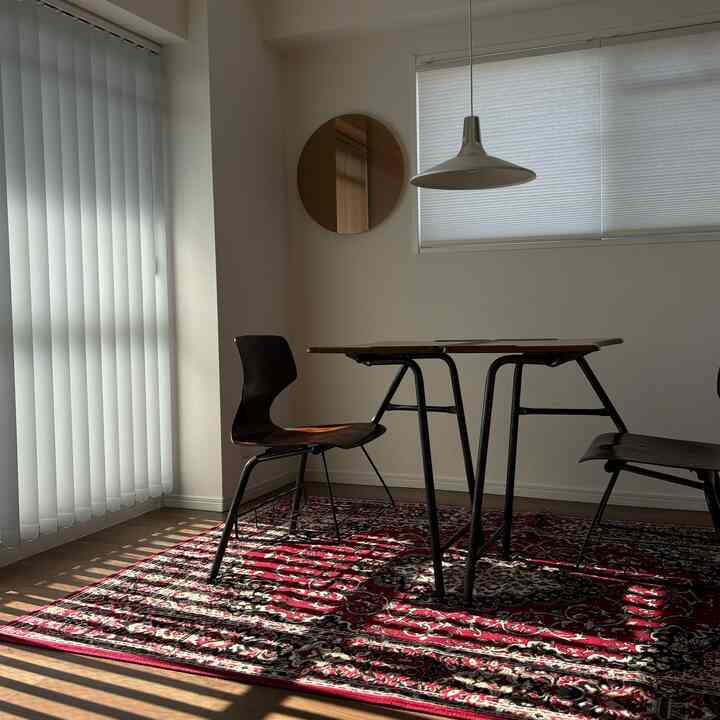 白い壁のミッドセンチュリーモダンなダイニング、赤いペルシャ絨毯と木製椅子が配置された印象的な空間