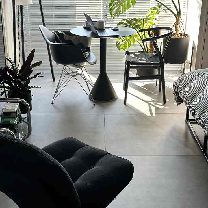 A small bedroom in white and gray tones featuring modern armchairs, a round dining table, and green plants as accents