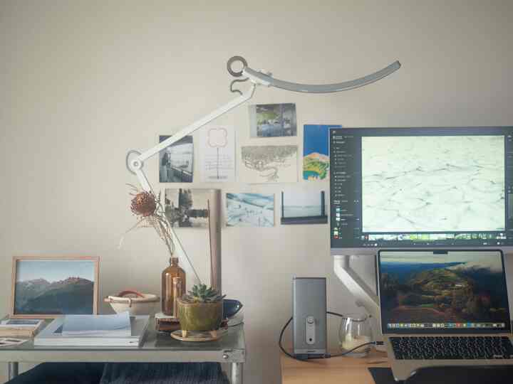 白い壁とブラウンの小物が調和したコンパクトなホームオフィス、机の上にLEDデスクランプとモニター、ノートパソコンが配置された雰囲気のあるインテリア