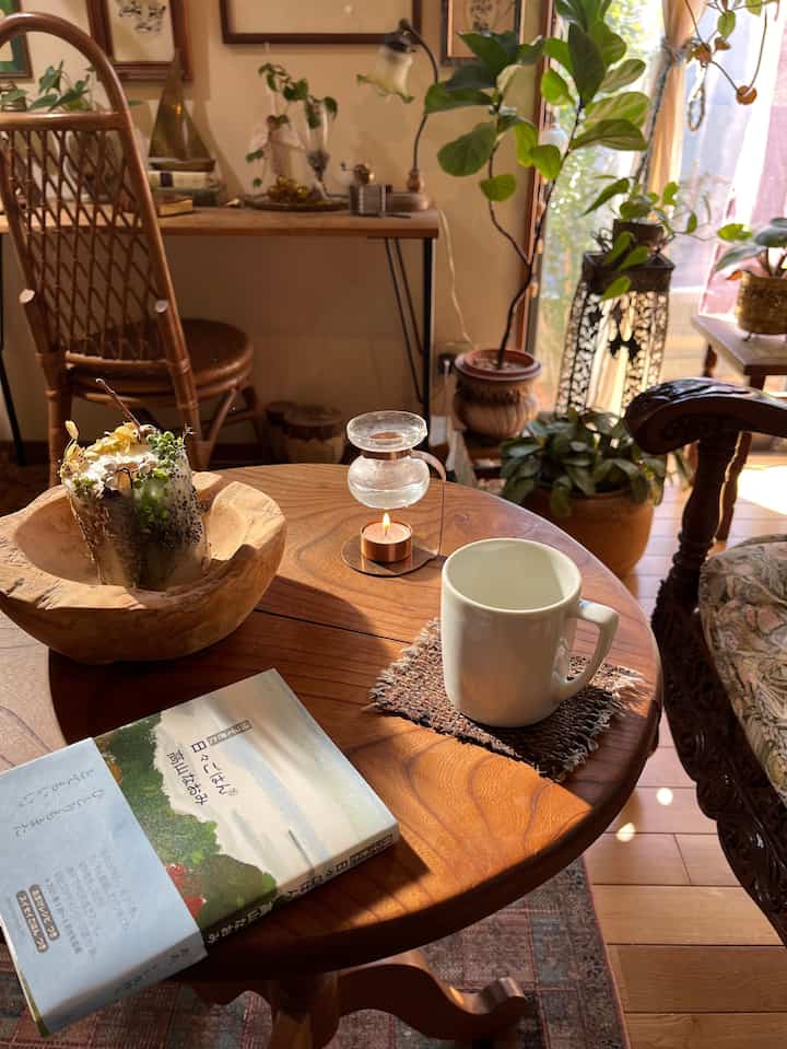 暖かい木目調と自然植物が調和した印象的なカフェ風リビング、中央の丸テーブルにはマグカップとキャンドルが置かれている