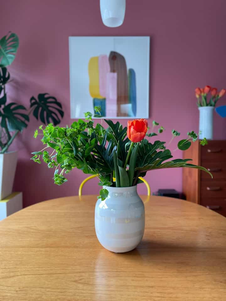 ピンクの壁と木製のダイニングテーブルに中央に白い花瓶と緑の植物が置かれた、雰囲気のあるダイニングルーム