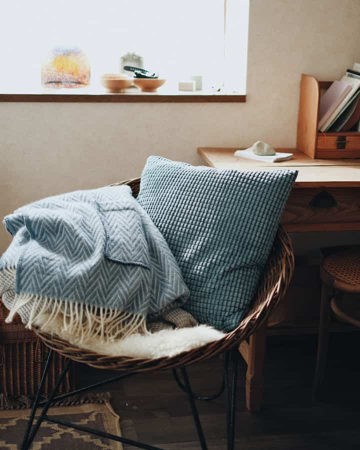 A small cozy room with natural colors and wood tones, featuring a rattan armchair with a blue cushion and blanket