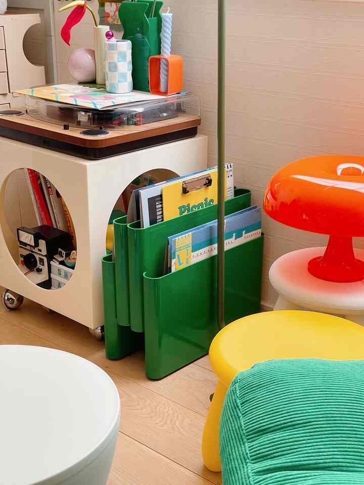 Colorful mid-century modern space dominated by green magazine rack, featuring retro table lamp and various stools with a vibrant atmosphere
