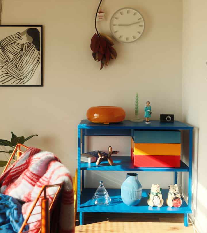 ナチュラルな色調の部屋に青い収納棚とオレンジ色の椅子が置かれたシンプルなインテリア空間