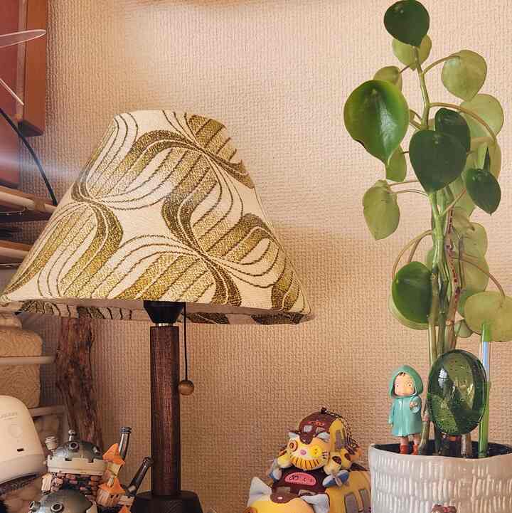 ベージュ色の壁とパターンのテーブルランプ、緑の植物と赤ちゃんのフィギュアが配置された、温かみのある自然なテーブル上のインテリア