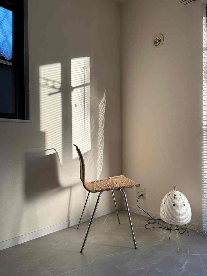 ベージュのナチュラルな色調のリビング、ラタンチェアと白いフロアランプが配置されたシンプルな空間