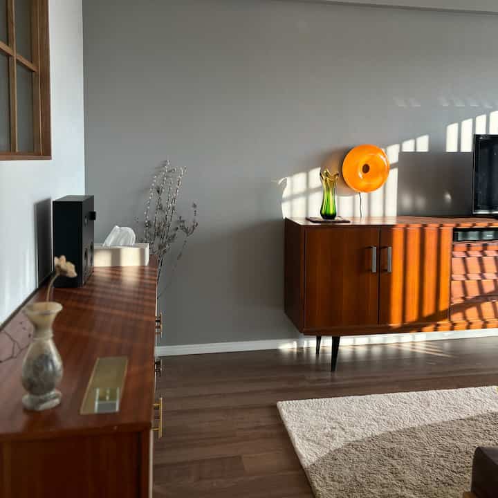 温かみのある木目調とグレーの壁が調和したミッドセンチュリーモダンのリビング、オレンジの照明がアクセントとなる空間