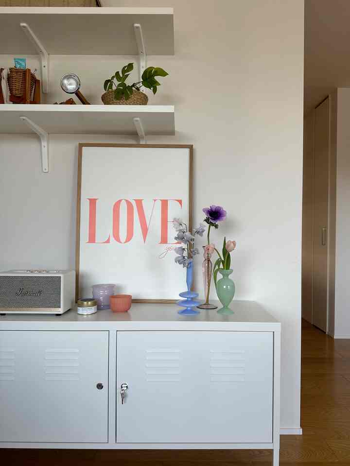 ホワイトとナチュラルカラーのミニマルスタイルのリビング、ホワイトのキャビネットと額縁、花瓶が配置された清潔感のある空間