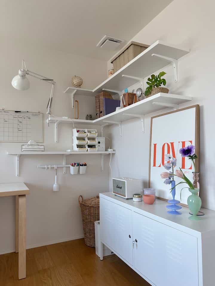 白とナチュラルカラーの小さなホームオフィス空間、壁の棚と収納家具が配置され、整然とした収納アイデアを表現