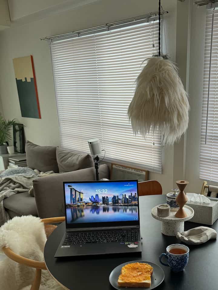 ベージュとブラックの色調の1LDKリビング兼ダイニングルーム、シンプルでミッドセンチュリーモダンなソファとダイニングチェア、ノートパソコンとブラインドが配置された印象的な空間