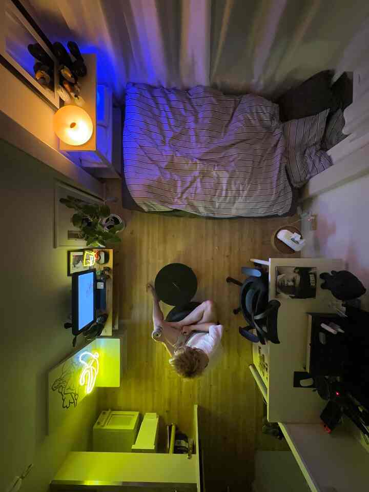 ナチュラルカラーの床とLED照明がある6畳のワンルーム、ベッドとデスク、オフィスチェアが配置されたコンパクトな一人暮らし空間