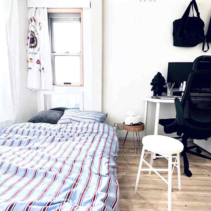 白と茶色のトーンが調和した6畳の寝室、ベッドとデスク、オフィスチェアが配置された整った一人暮らし空間