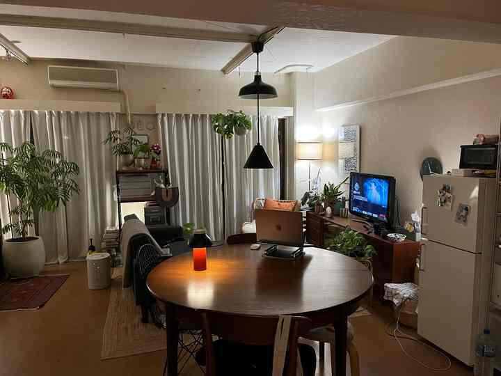 Warm wood-tone two-person living room featuring round dining table and sofa amidst plants creating cozy atmosphere