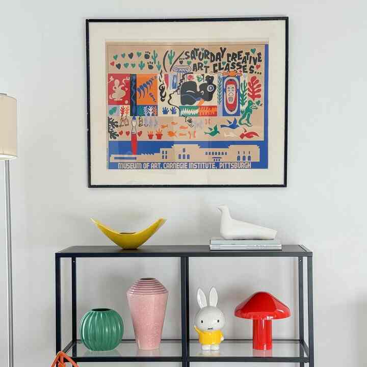 白い壁と黒のメタルシェルフがあるリビング、カラフルでヴィンテージ風の花瓶とオブジェが配置された雰囲気のあるインテリア