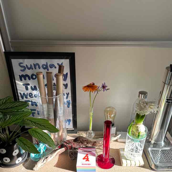 ナチュラルな色調のディスプレイラックにカレンダーと花、コーヒーマシンが配置された印象的なホームカフェ空間