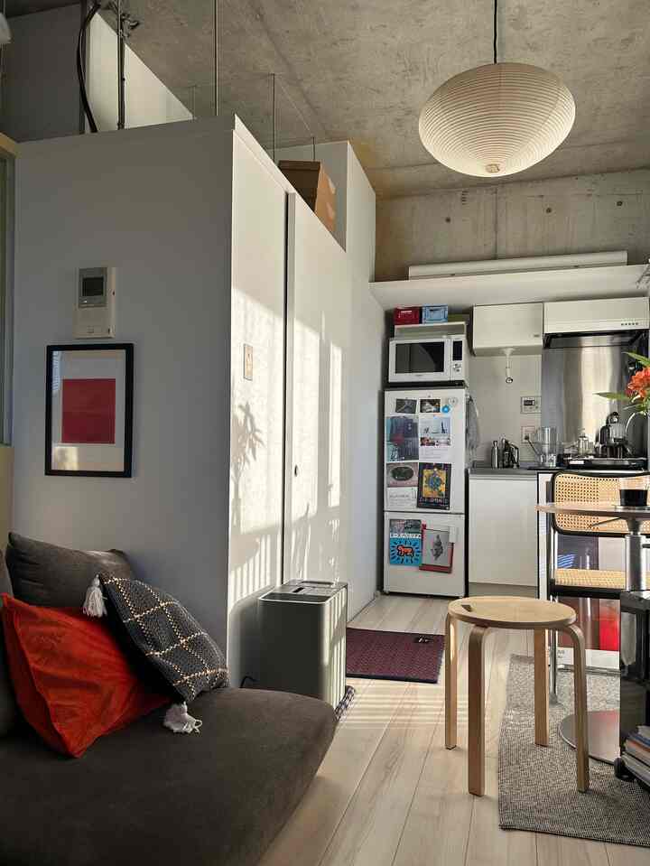 白い壁とナチュラルな木目調の床、コンパクトなワンルームにブラウンのソファとラタンのダイニングチェアが配置された雰囲気のあるインテリア