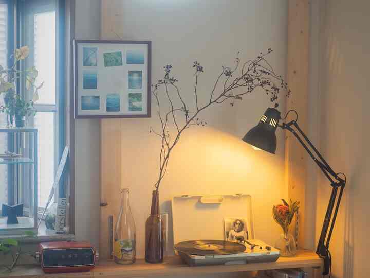 温かみのある木目調と黒いデスクライトが配置された一人暮らしの壁面棚と額縁のある雰囲気の良いインテリア