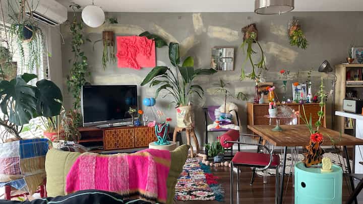 ナチュラルトーンと緑の植物が調和したリビング、ヴィンテージ家具とカラフルな小物が配された雰囲気のあるインテリア