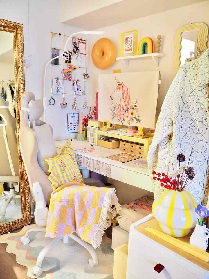 ラベンダーとオレンジのチェック柄ブランケットをかけた椅子と白いデスクがある明るいホームオフィス