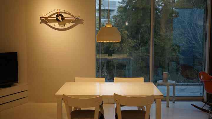 ホワイトトーンとナチュラルカラーが調和するダイニング、アルテック家具、ヴィトラの時計、ペンダントライトが配置されたモダンなインテリア