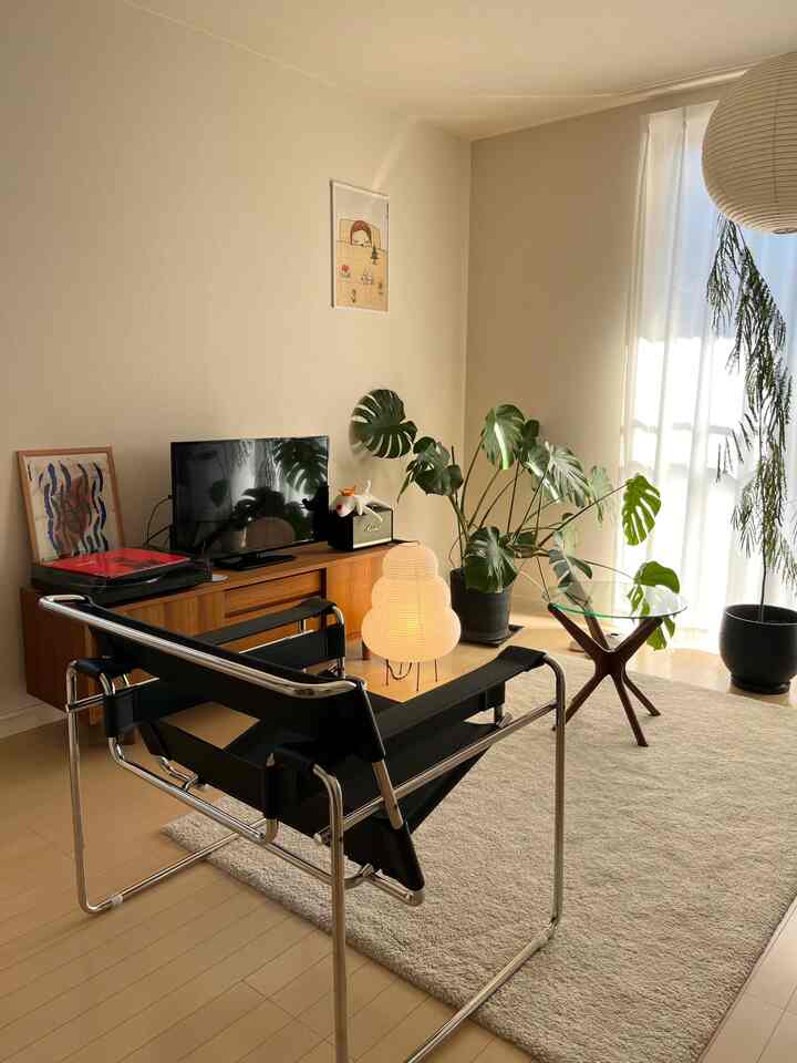 明るいナチュラルカラーのリビング、モダンなアームチェアとアカリのフロアランプ、大きなラグ、緑豊かな植物が配置された雰囲気のある空間