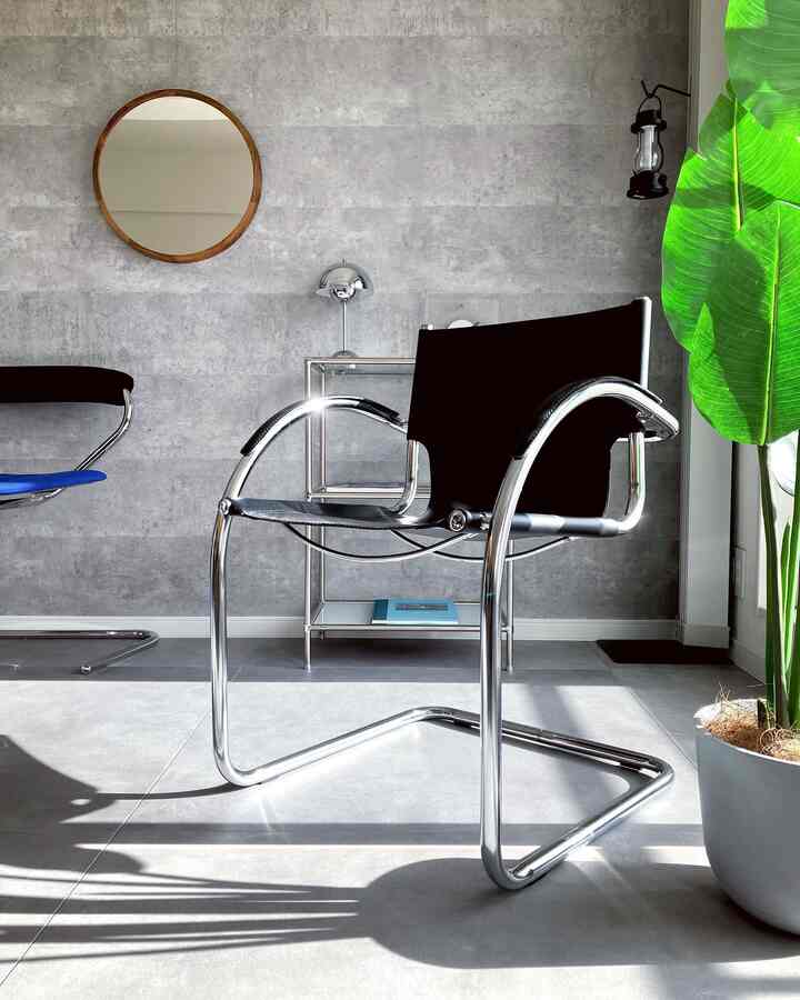 グレーの無機質な壁と木枠の丸い鏡、クロームフレームの黒い椅子が配置されたシンプルなインテリア