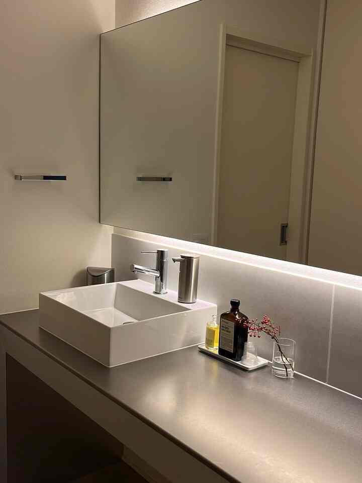 シルバートーンの洗面台と間接照明が配置されたシンプルで清潔感のあるバスルーム